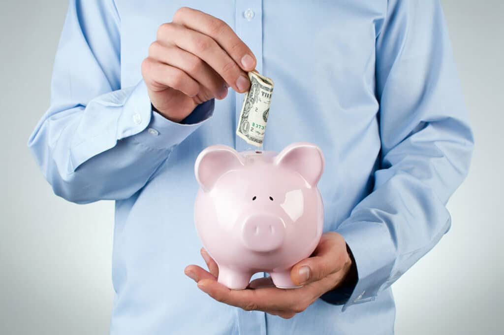 Client Story - Changes in health and Home - man in light blue shirt putting dollar bill in pink piggy bank